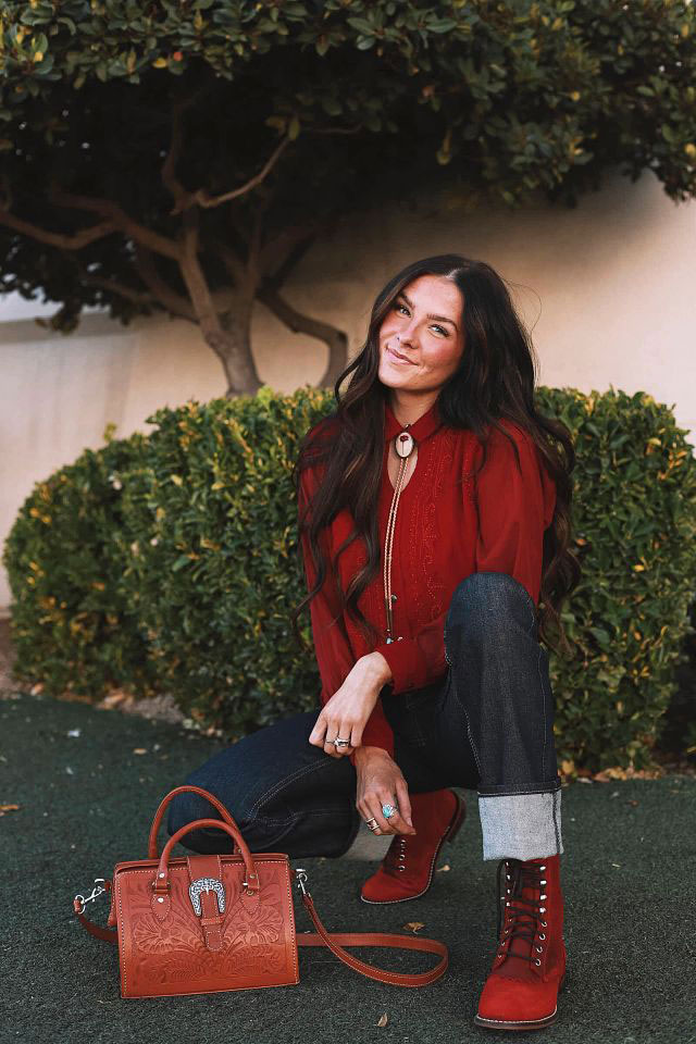 A woman wearing Justin boots kneeling into of a bush.